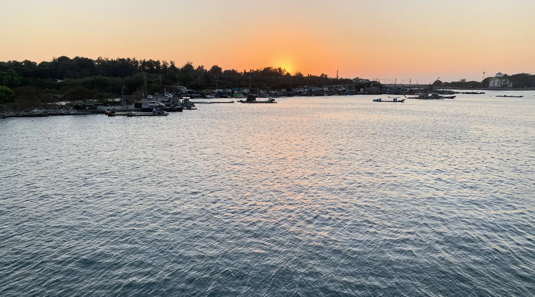 夕陽下的海面，遠處是漁港和停泊的小船
